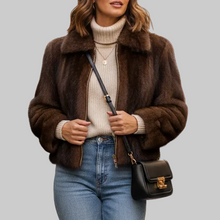 Įkelti nuotrauką į galerijos peržiūros programą, A woman wearing a brown faux fur jacket over a cream turtleneck sweater and blue jeans, carrying a black leather shoulder bag with gold hardware on a blurred city street.