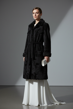 Įkelti nuotrauką į galerijos peržiūros programą, A woman stands in a studio wearing a long black textured coat over a flowing white skirt, holding a small white clutch against a gray background with dramatic side lighting.
