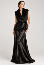Load image into Gallery viewer, A woman models a black faux fur wrap vest with a matching fabric tie belt, paired with a long black satin maxi skirt, against a light gray studio background.