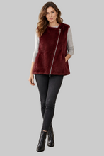 Load image into Gallery viewer, A woman modeling a sleeveless burgundy faux fur vest with a front zipper over a light gray long-sleeve top, black skinny jeans, and black ankle boots, set against a solid gray background.