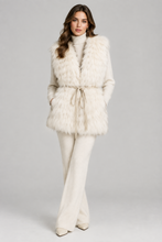 Load image into Gallery viewer, A woman models a cream-colored faux fur vest with a tie belt over a matching cream knit turtleneck and wide-leg pants, set against a solid light gray studio background.