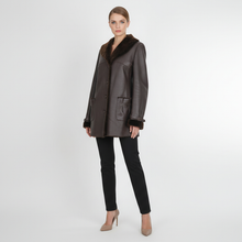 Įkelti nuotrauką į galerijos peržiūros programą, A woman modeling a dark brown leather jacket with a contrasting dark brown fur collar, paired with black pants and beige heels, against a light gray studio background.