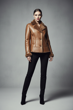 Įkelti nuotrauką į galerijos peržiūros programą, A model stands against a gray studio background wearing a tan leather jacket with a brown fur collar and lining, paired with black pants and black ankle boots.