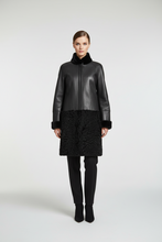 Load image into Gallery viewer, A model stands against a light gray studio background wearing a black leather and textured black outerwear piece with a high collar, black pants, and black ankle boots.