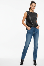 Load image into Gallery viewer, A woman modeling a sleeveless black leather-look top and blue jeans against a plain white studio background.