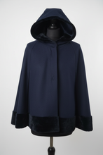 Load image into Gallery viewer, A navy blue hooded cape jacket with dark plush faux-fur trim on the hood, cuffs, and hem, displayed on a black mannequin torso against a light gray background.