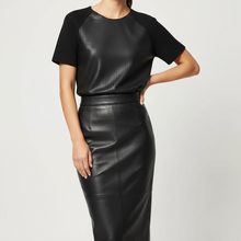 Load image into Gallery viewer, A woman modeling a black short-sleeve top with textured raglan sleeves and a black faux-leather pencil skirt, photographed against a light gray studio background.