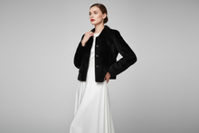 Įkelti nuotrauką į galerijos peržiūros programą, A model wearing a black velvet cropped jacket over a long white dress, standing against a neutral gray studio background.