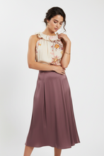 Load image into Gallery viewer, A woman modeling a sleeveless ruffled blouse with a floral print and a pleated midi skirt in dusty mauve, photographed against a clean light gray studio background.