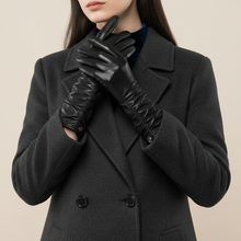 Įkelti nuotrauką į galerijos peržiūros programą, A woman wearing a dark charcoal gray wool coat and long black leather gloves, holding them up in front of her chest against a solid beige background.