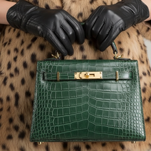 Įkelti nuotrauką į galerijos peržiūros programą, A green crocodile-embossed leather handbag held by a person wearing black leather gloves and a leopard-print faux fur coat, against a plain light gray background.