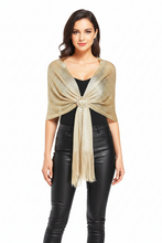 Įkelti nuotrauką į galerijos peržiūros programą, A woman modeling a shimmering gold knit wrap shawl with fringe and a decorative circular center detail, styled over a black top and black faux-leather pants against a plain white background.