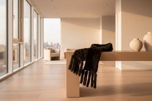 Load image into Gallery viewer, Modern interior with a black scarf draped over a wooden bench, large windows, and cityscape view.