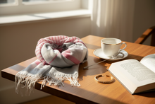 Load image into Gallery viewer, Scarf, cup of tea, and open book on a wooden surface with sunlight streaming in.