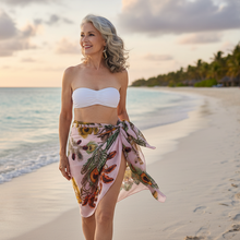 Įkelti nuotrauką į galerijos peržiūros programą, Woman in a white strapless top and floral skirt standing on a beach with ocean and palm trees in the background.