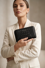 Load image into Gallery viewer, A woman in a cream-colored blazer holds a black crocodile-embossed wallet by Balenciaga. The brand name 'BALenciaga' is clearly embossed on the front of the wallet.