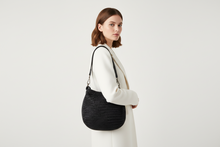 Load image into Gallery viewer, Woman holding a black woven handbag against a plain background