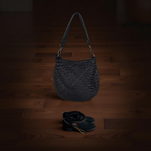 Load image into Gallery viewer, Black woven handbag on a wooden floor with a dark background