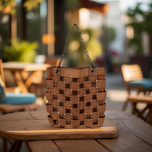 Load image into Gallery viewer, Brown woven handbag on a wooden table with a blurred outdoor background