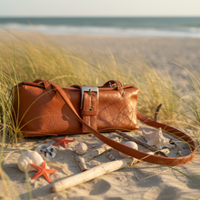 Load image into Gallery viewer, Brown leather bag on a sandy beach with seashells and starfish