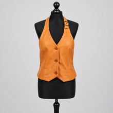 Įkelti nuotrauką į galerijos peržiūros programą, An orange leather halter vest with a button front and a decorative buckle strap on the shoulder, displayed on a black mannequin torso against a light gray background.