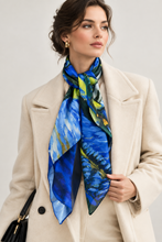 Load image into Gallery viewer, A woman wearing a cream-colored coat and a vibrant blue and green abstract-patterned silk scarf, photographed against a neutral light gray background.