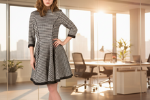 Load image into Gallery viewer, Woman in a checkered dress standing in an office with large windows.