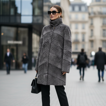 Įkelti nuotrauką į galerijos peržiūros programą, A woman stands on a city street wearing a gray textured faux-fur turtleneck coat with geometric paneling, black pants, black ankle boots, and carrying a black handbag.