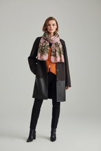 Įkelti nuotrauką į galerijos peržiūros programą, A model stands against a light gray studio background wearing a dark brown coat with black leather-look lower panels, a pink scarf with a botanical print, an orange top, black pants, and black ankle boots.