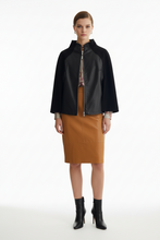 Load image into Gallery viewer, A model stands against a white studio background wearing a black leather cape jacket with a high collar and a front zipper, paired with a brown pencil skirt and black ankle boots.