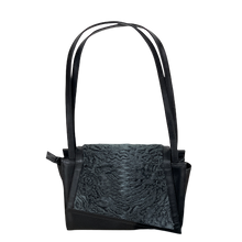 Load image into Gallery viewer, A black leather handbag with astrakhan fur detailing, featuring a textured design, a zippered compartment, and two handles.