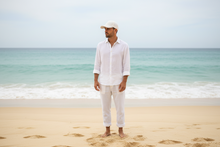 Load image into Gallery viewer, Man in white outfit standing on a beach with clear blue sky and ocean.