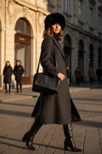 Load image into Gallery viewer, Woman in a long dark coat and fur hat walking on a city street.