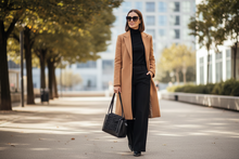 Load image into Gallery viewer, Woman in a tan coat and black outfit walking on a city street.