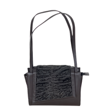 Load image into Gallery viewer, A black handbag featuring high-quality astrakhan fur on the front and two handles. The bag has a closure with magnetic snaps and an additional zippered compartment, indicating interior pockets for organization.