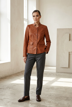 Įkelti nuotrauką į galerijos peržiūros programą, A woman stands in a bright, minimalist studio wearing a cropped brown leather jacket, dark gray trousers, and dark brown leather loafers.