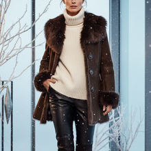 Load image into Gallery viewer, A woman walks through a snowy modern glass corridor wearing a dark brown fur-trimmed coat over a cream ribbed turtleneck sweater, black leather pants, and black knee-high boots.