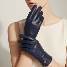 Įkelti nuotrauką į galerijos peržiūros programą, A model wearing navy blue leather gloves, with one glove held up to show the back and the other resting on the forearm. The model is wearing a cream-colored sleeveless top against a neutral light gray background.
