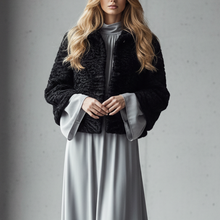 Įkelti nuotrauką į galerijos peržiūros programą, A woman stands in a minimalist concrete room wearing a black textured cropped jacket over a gray mock-neck top and a long flowing light gray skirt.