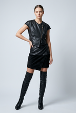 Load image into Gallery viewer, A model wearing a black faux-leather sleeveless top with a front zipper, a matching black velvet wrap mini skirt, and black over-the-knee boots, posed against a light gray studio background.