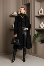 Įkelti nuotrauką į galerijos peržiūros programą, A long black textured faux fur coat with a wide collar and long sleeves, displayed on a black mannequin against a light gray background.