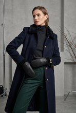 Įkelti nuotrauką į galerijos peržiūros programą, A woman models a long navy wool-blend coat with a dark fur collar, paired with a black turtleneck, dark green trousers, black gloves, and gold buttons, set against a gray studio backdrop.