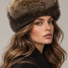 Load image into Gallery viewer, A close-up portrait of a woman wearing a luxurious brown and black fur ushanka hat, with wavy light brown hair and a neutral gray background.