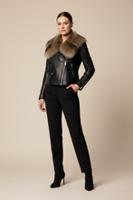 Įkelti nuotrauką į galerijos peržiūros programą, A model stands against a solid beige studio background wearing a black leather moto jacket with a large brown fur collar, black trousers, and black high-heeled boots.