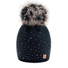 Load image into Gallery viewer, A black knitted cap with a grey artificial fur pom-pom and Swarovski crystals, featuring a small brown label with a brand logo.