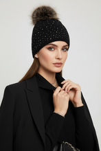 Įkelti nuotrauką į galerijos peržiūros programą, A woman wearing a black knit beanie with small silver rhinestone-like dots and a large brown faux-fur pom-pom, styled with a black blazer against a light gray studio background.