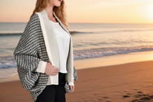Load image into Gallery viewer, Woman standing on a beach at sunset wearing a checkered jacket.