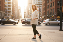Load image into Gallery viewer, Woman walking on a city street with tall buildings in the background