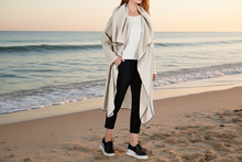 Load image into Gallery viewer, Woman standing on a beach wearing a light-colored linen long cardigan, white shirt, black pants, and black shoes.