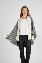 Load image into Gallery viewer, A woman modeling a black and white houndstooth cape cardigan with a solid cream collar, worn over a white top and black faux-leather pants against a plain white background.